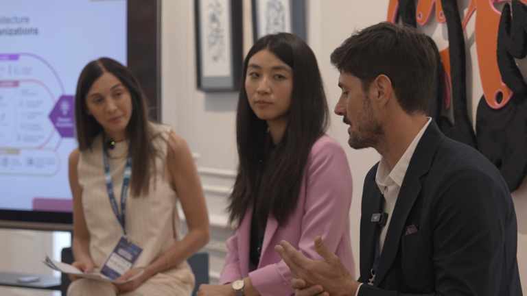 Three speakers discussing topics on a panel in an artistic setting, with a presentation backdrop.
